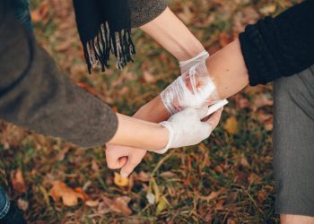 Providing first aid in the park. Man bandaged injured arm. Guy helps a friend.